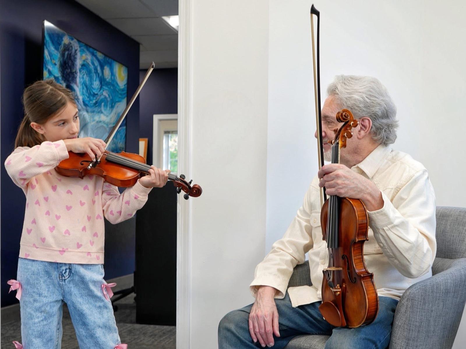 A young violinist playing while her teacher listens, his own violin in hand